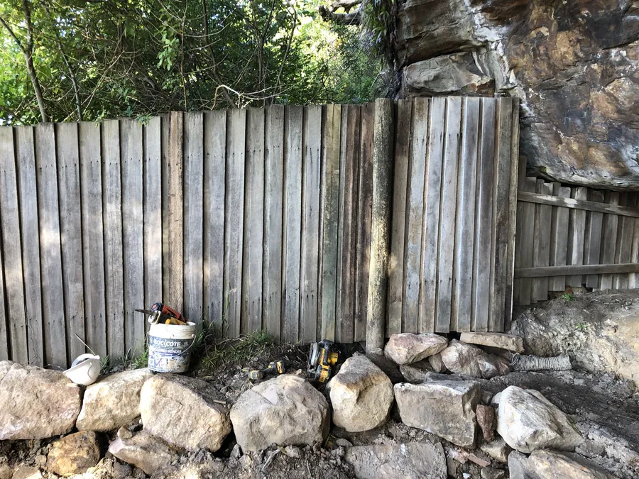 Paling fence run rebuilt with new palings against sandstone