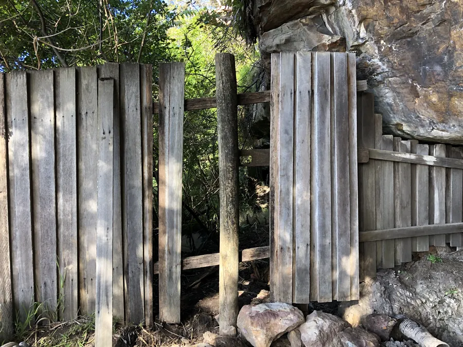 Timber paling fence with a section of palings missing and a leaning post