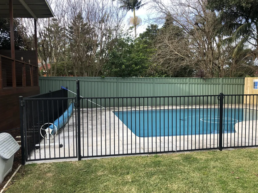 Black aluminium pool fence and gate beside a lawn, pool behind